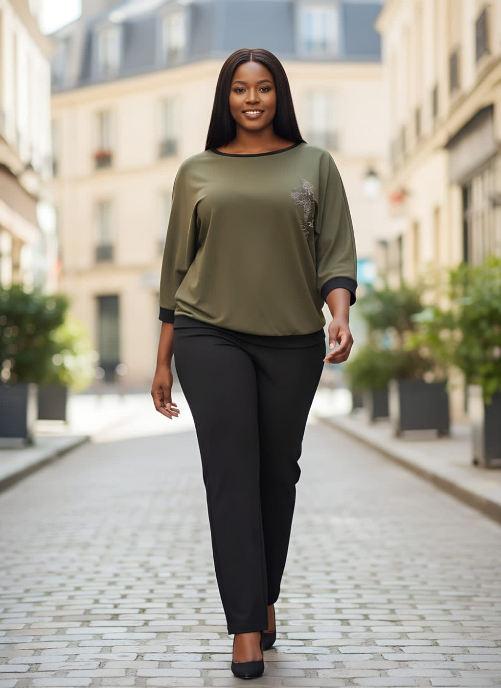Woman walking on a city street wearing an olive green top and black pants.
