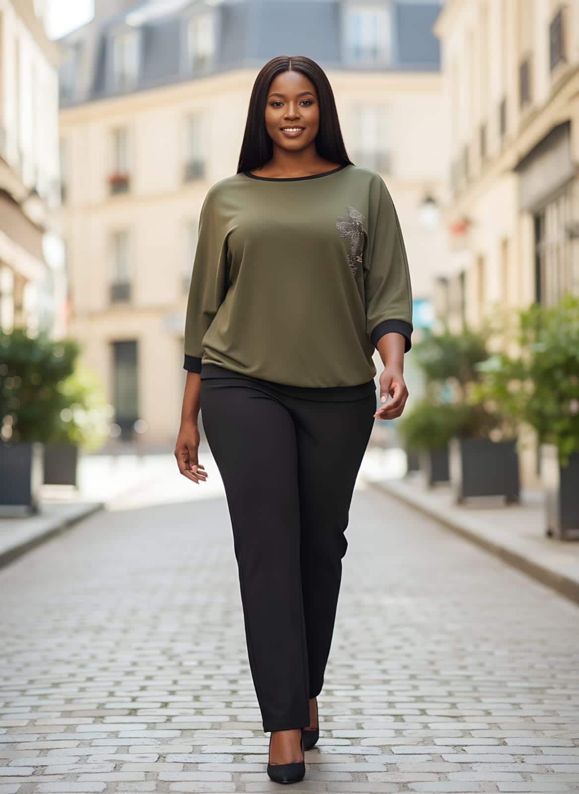 Woman walking on a city street wearing an olive green top and black pants.